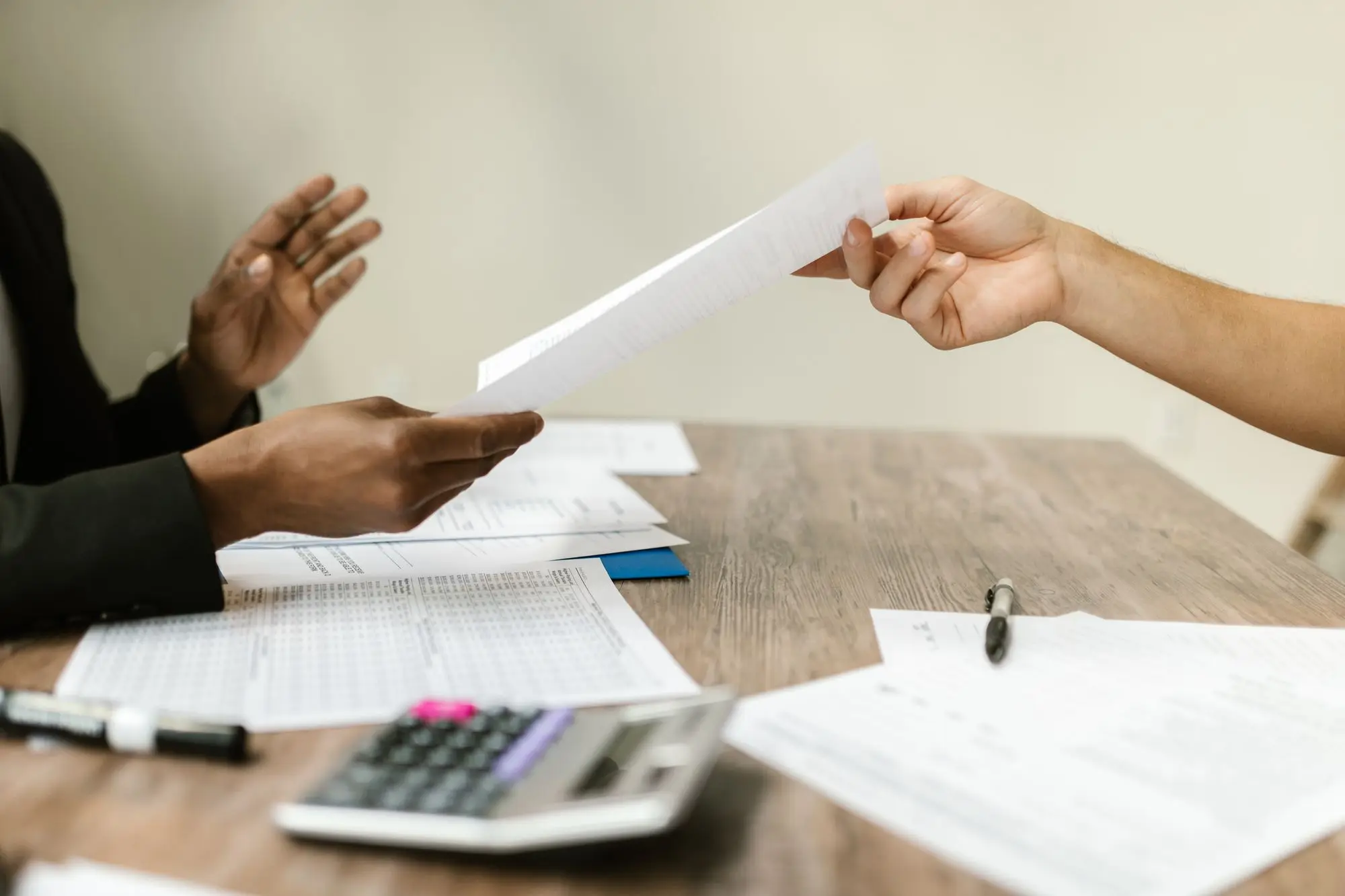 Seller passing a signed sale contract across a desk to a buyer, with a calculator and financial statements on the table